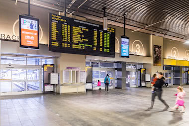 People walking by train departure board inside North Station