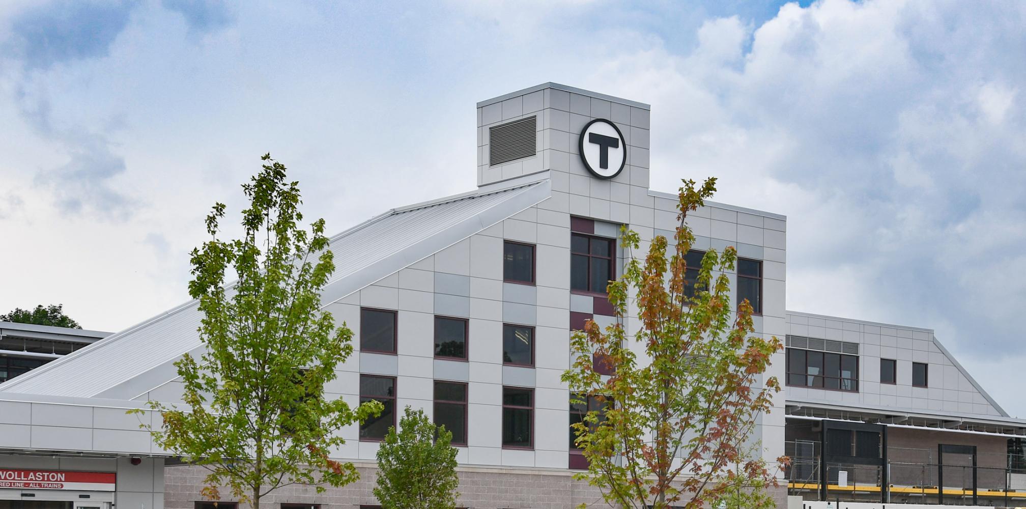 Renovated Wollaston Station, viewed from the parking lot, with trees. (August 7, 2019)