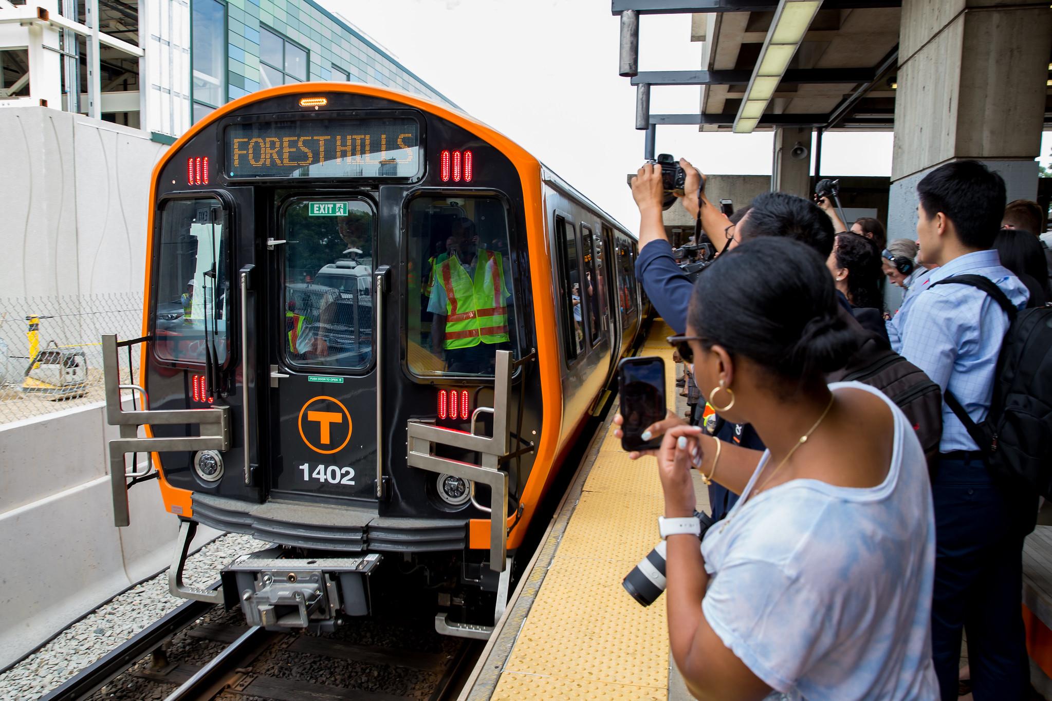 New Orange Line car at Wellington, as a crowd on the platform takes photos.