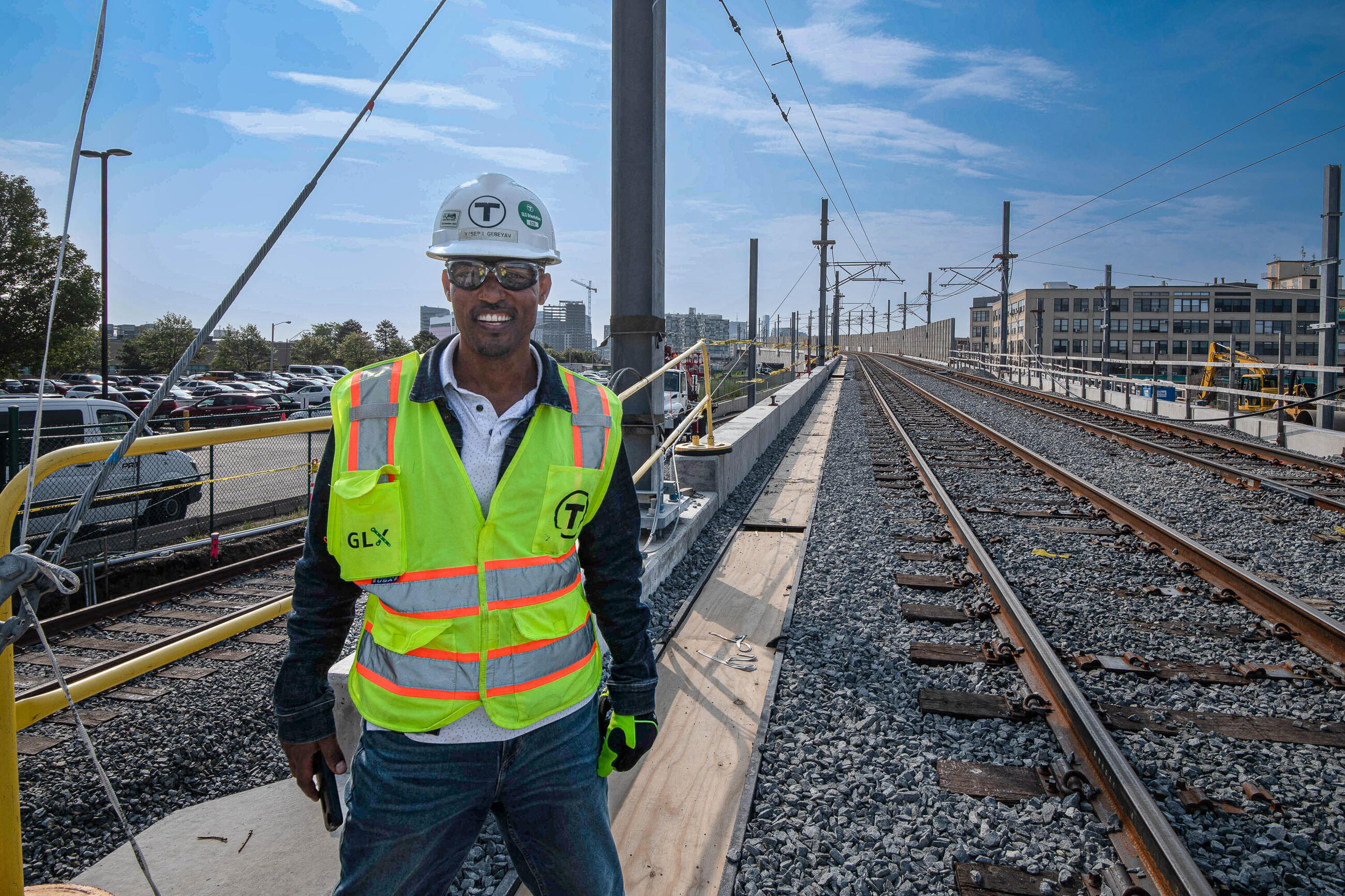 A GLX inspector in a hard hat and high vis vests smiles next to new train tracks