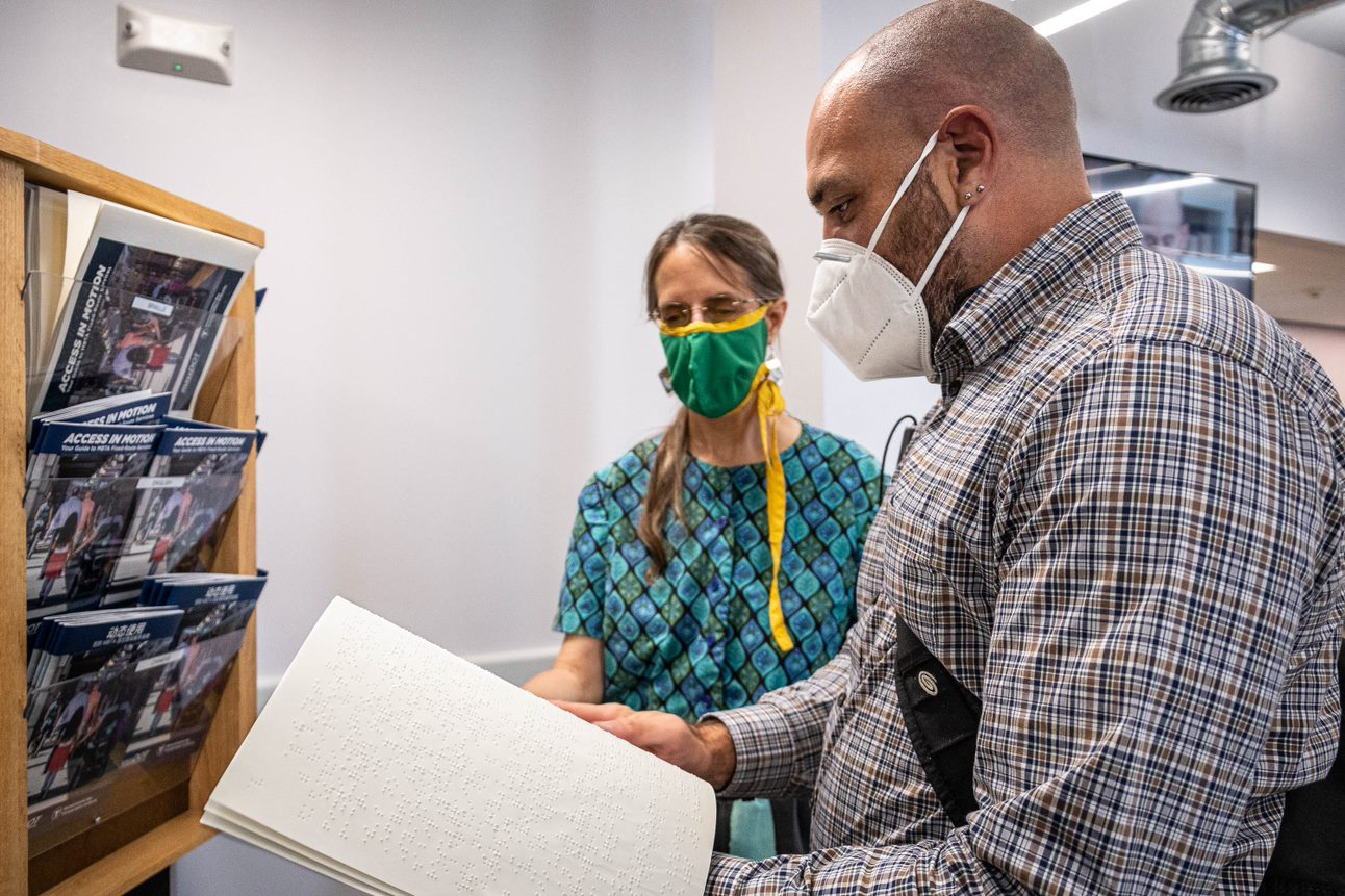 Rider reading through Access in Motion guide in Braille with guidance from employee