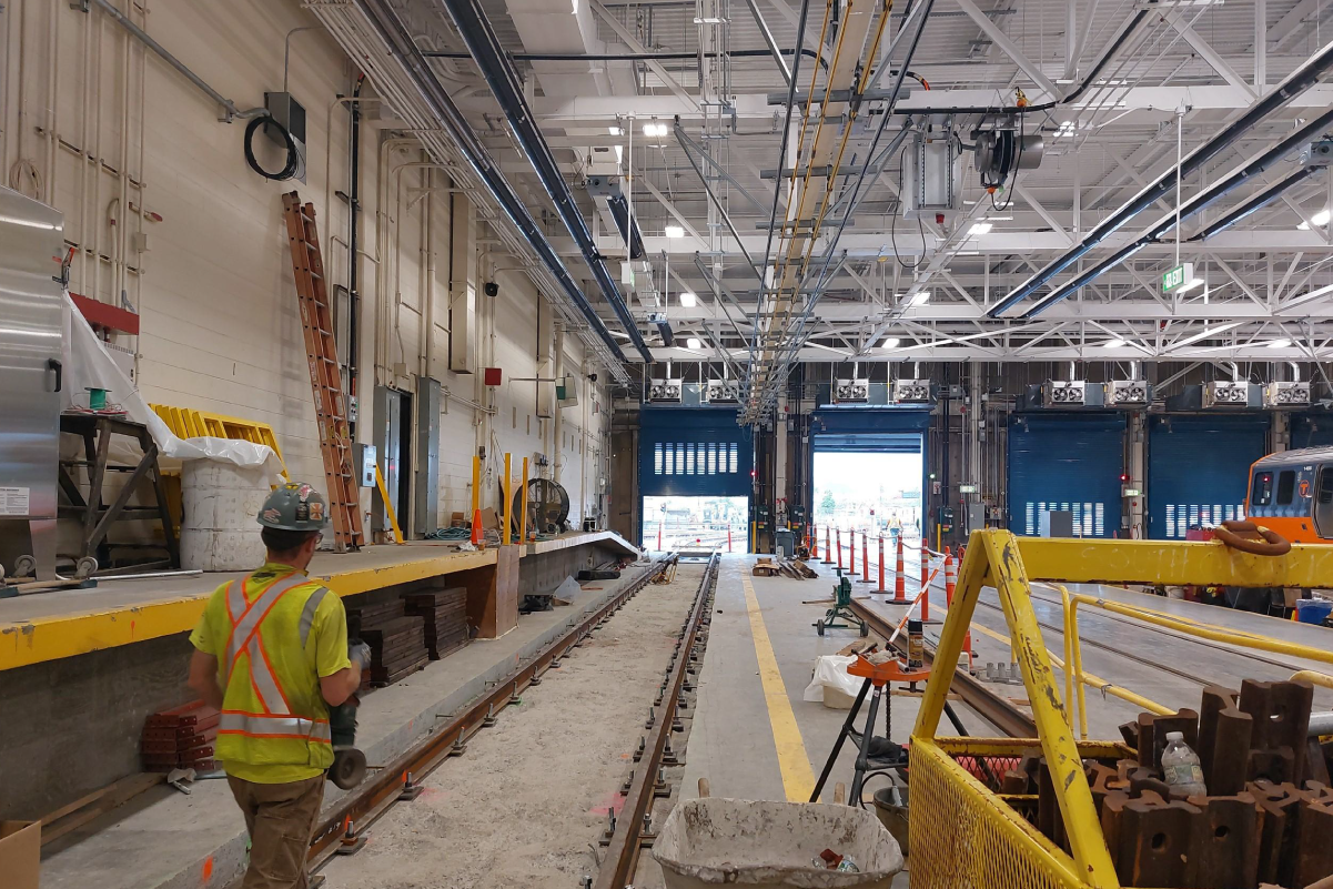 crew member standing on maintenance tracks inside a large bright warehouse type facility